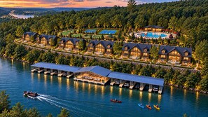 Un complexe hôtelier au bord d’un lac, comprenant plusieurs chalets, une piscine et des bateaux amarrés.