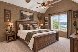 Un dormitorio con ventilador de techo de madera, una cama grande con vista a un lago y una ventana con cortinas.