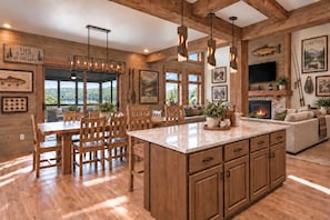 A spacious kitchen with a large island, wooden dining area, and a cozy living space with a fireplace. - Branson Golf Trip Retreat | 4BR Lake Lodge + Pool, Chip & Putt Course! (Hollister)