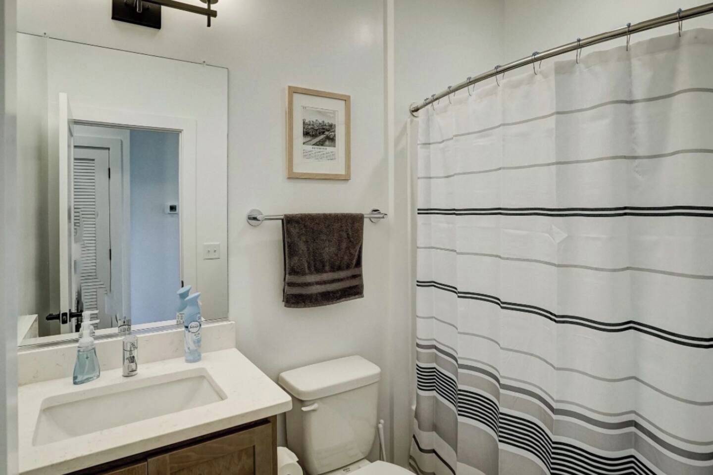 A bathroom with a sink, mirror, toilet, towel rack, and striped shower curtain.