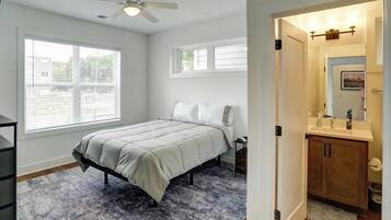 A bedroom with a bed, a ceiling fan, a window, and a bathroom with a sink and cabinet.