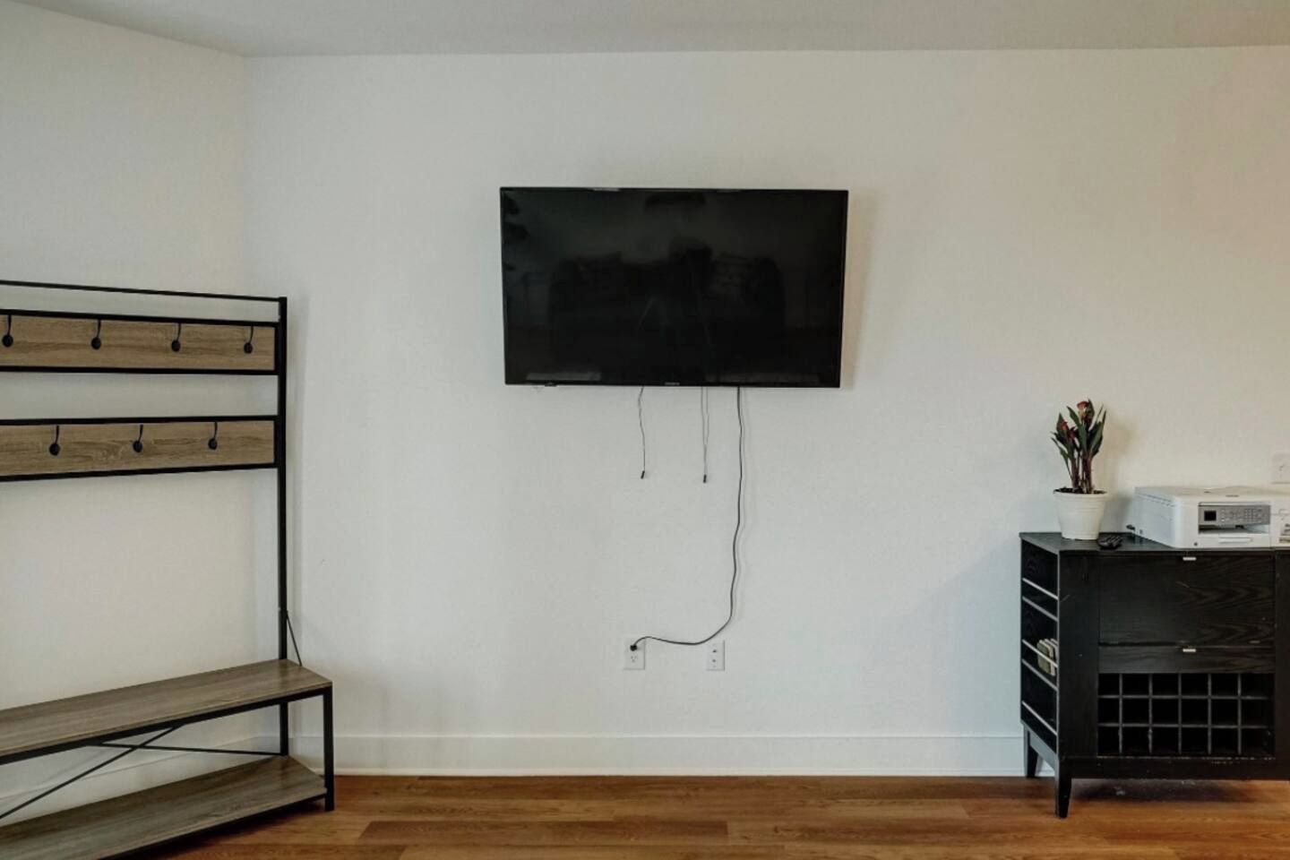 Habitación con televisor de pantalla plana montado, un banco de madera y un mueble de entretenimiento negro con dispositivos electrónicos.