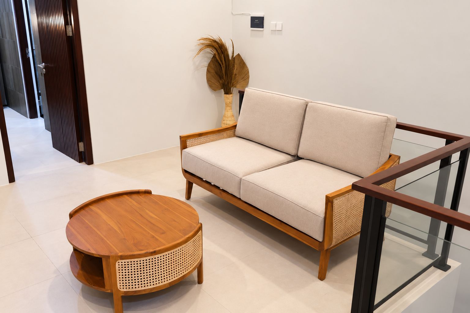 Una sala moderna con un sofá, una mesa de centro redonda de madera y un jarrón decorativo con plantas secas.