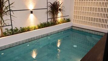 An indoor swimming pool with a tiled edge, surrounded by a white wall with black grid patterns and a white lattice panel.