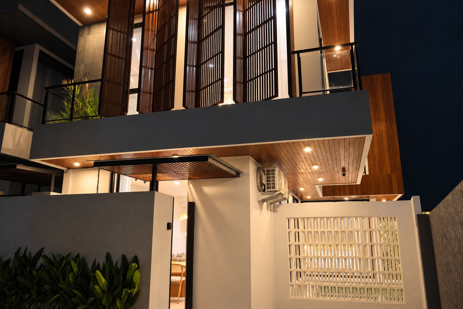 Un edificio moderno de varios pisos con un balcón, una zona de estar al aire libre techada y una pared blanca con un panel decorativo.