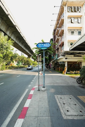 A street with a blue directional sign, a sidewalk, and a building with multiple floors. - L room Sukhumvit 42 (Bangkok)