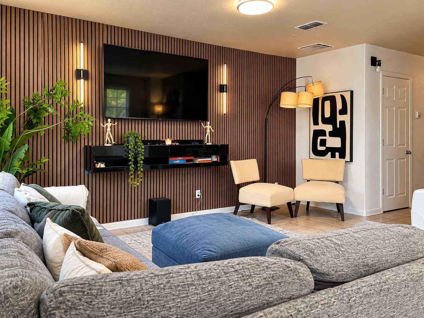 Una sala de estar moderna con un televisor de pantalla plana grande, una pared de acento de madera, un sofá, una mesa de centro y un par de sillones.