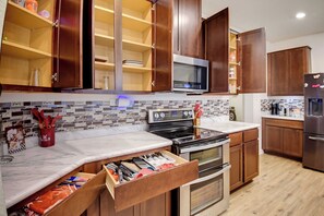 A kitchen with wooden cabinets, a microwave, a stove, and a refrigerator. - Game Night HQ! Arcade, Pool Table & 5BR (Seguin)