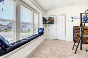 A room with a window seat, a television, and a door with a gaming-themed decoration. - Game Night HQ! Arcade, Pool Table & 5BR (Seguin)