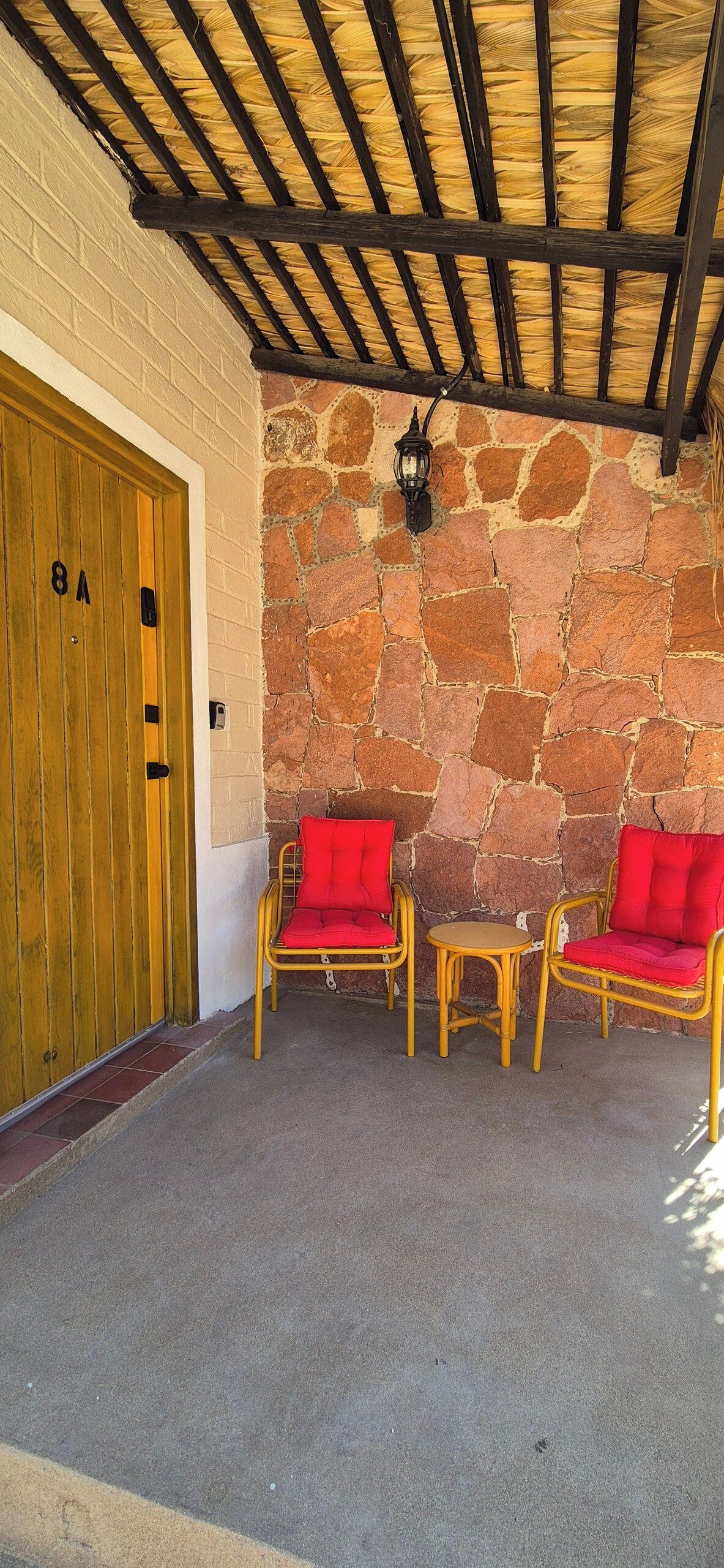 Un área de estar al aire libre con techo, paredes de piedra y una puerta de madera que indica '8A'.