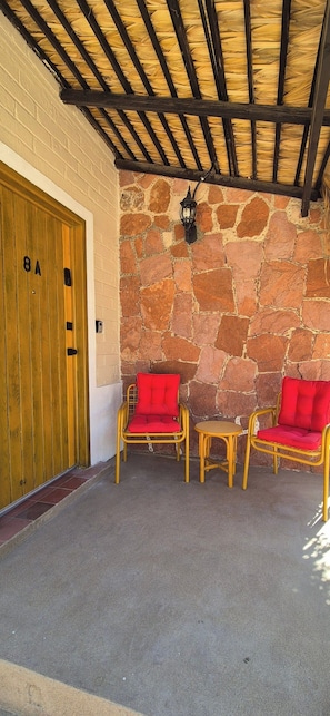 Uma área de estar coberta ao ar livre, com paredes de pedra e uma porta de madeira com a inscrição '8A'.
