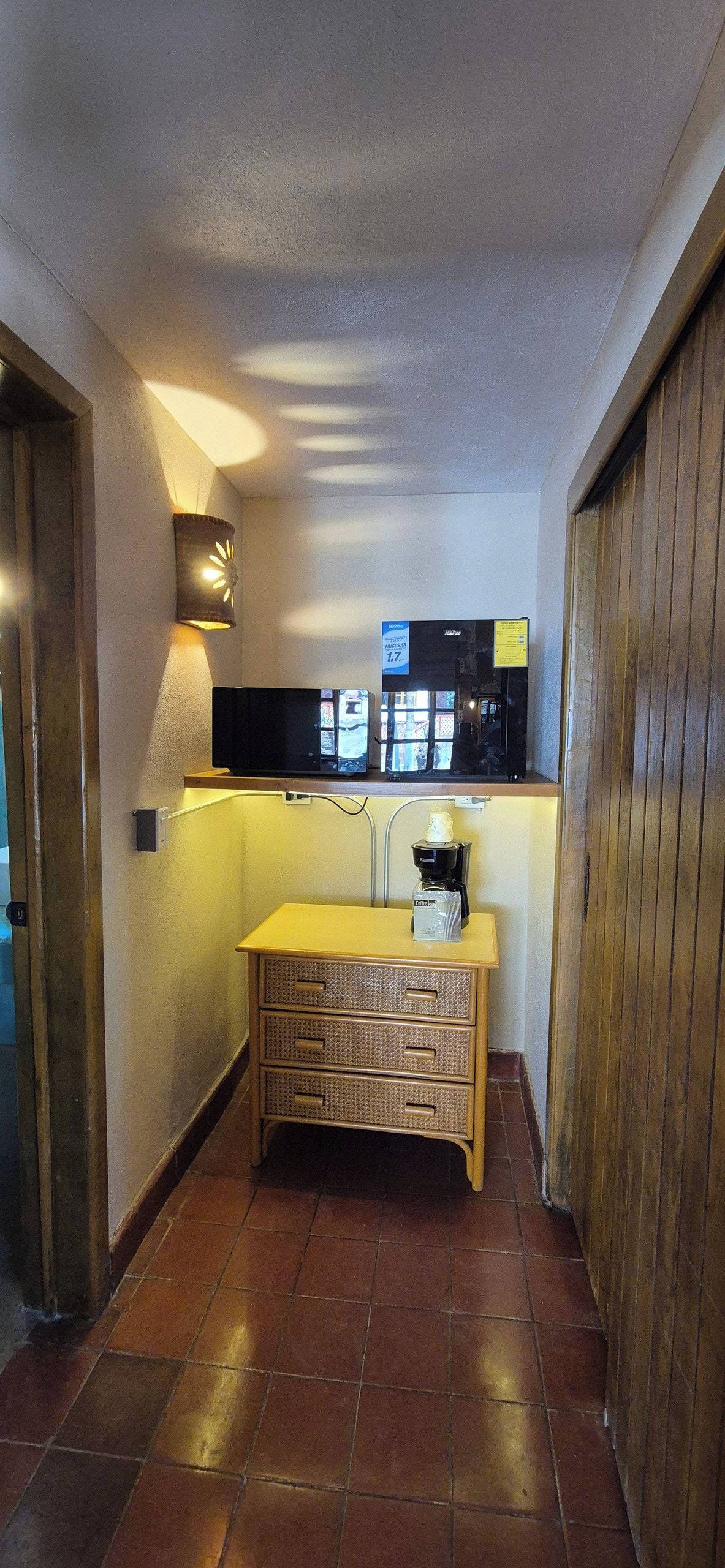 Un pasillo estrecho con un banco de madera, una máquina de café y un televisor montado en la pared.