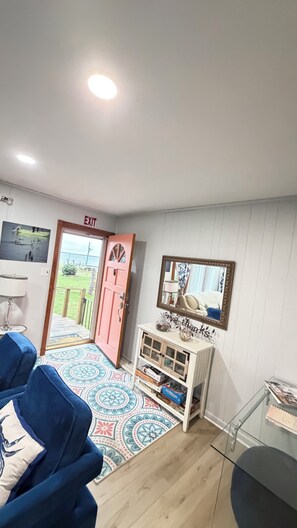 A room with a blue sofa, a patterned rug, a white cabinet with glass doors, and a door leading outside. - River Retreat dogs welcome amazing views & sunnroom (Hague)