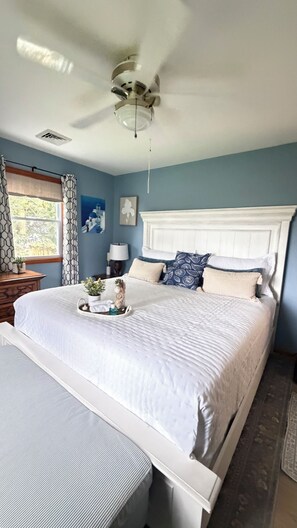 A bedroom with a large bed, a ceiling fan, a window with curtains, and a nightstand with a lamp. - River Retreat dogs welcome amazing views & sunnroom (Hague)