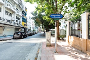 Une rue bordée de voitures garées, un panneau de signalisation bleu et un immeuble doté de balcons.