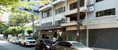 A multi-story residential building with balconies, parked cars, and a sidewalk.