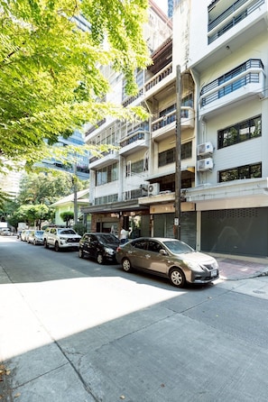 Un immeuble résidentiel à plusieurs étages, doté de balcons, avec des voitures garées et un trottoir.