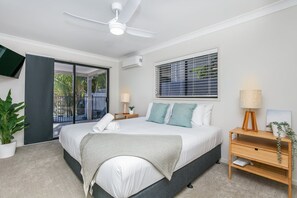 Une chambre à coucher moderne avec un lit, des tables de chevet, un ventilateur de plafond, une fenêtre avec des stores et une plante en pot.