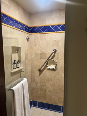 Un baño con ducha, un pasamanos, un perchero y un estante con artículos de aseo.
