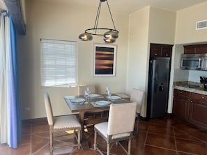 Un comedor con una mesa dispuesta para cuatro, un refrigerador y un microondas en la cocina contigua.