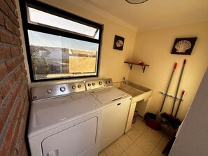 Un espace buanderie équipé d’un lave-linge et d’un sèche-linge, une fenêtre avec vue et un évier.