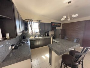 Une cuisine moderne avec des meubles de couleur sombre, un îlot central et un coin repas avec des chaises.