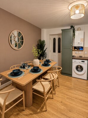 A dining area with a wooden table set for six, surrounded by four chairs. A washing machine is visible in the background. - Stylish  4BR Home | Perfect for Contractors (Bishop Auckland)