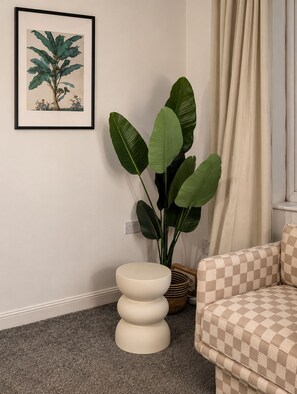 A room with a large potted plant, a framed botanical illustration, a checkered sofa, and a white bowl on a stand. - Stylish  4BR Home | Perfect for Contractors (Bishop Auckland)