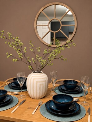 A dining table set with dark blue plates, a striped vase with branches, and a round mirror on the wall. - Stylish  4BR Home | Perfect for Contractors (Bishop Auckland)