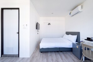 Habitación de hotel con cama, escritorio, silla, aire acondicionado, televisor y puerta.