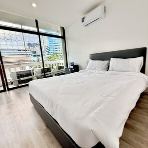Habitación de hotel moderna con una cama grande, una mesita de noche y vistas de la ciudad a través de ventanales del suelo al techo.