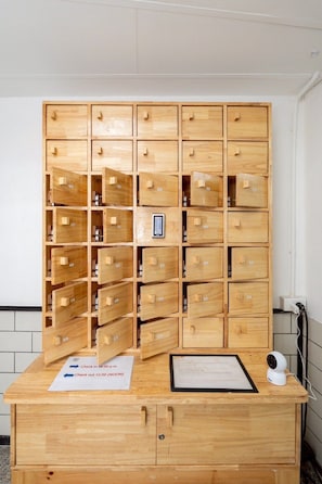 A wooden storage unit with multiple compartments, a small electronic device, and a sign with check-out times. - T room Silom4 (Bangkok)
