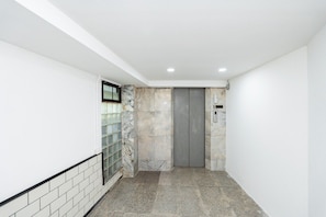 A hallway with a tiled floor, a marble wall, and a grey elevator door. - T room Silom4 (Bangkok)