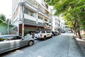 A street with parked cars, a white police car, and multi-story residential buildings. - T room Silom4 (Bangkok)