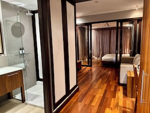 A hotel room with a wooden floor, a bed, a sitting area, and a bathroom with a shower. - H room De Silom (Bangkok)