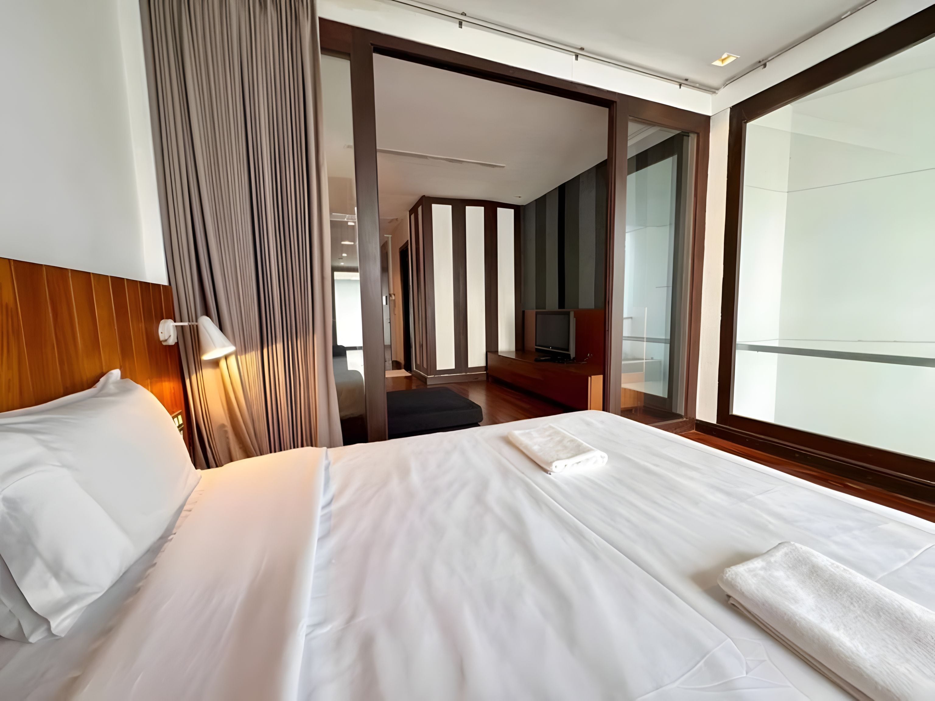 A hotel room with a bed, a TV, a desk, and a large window.