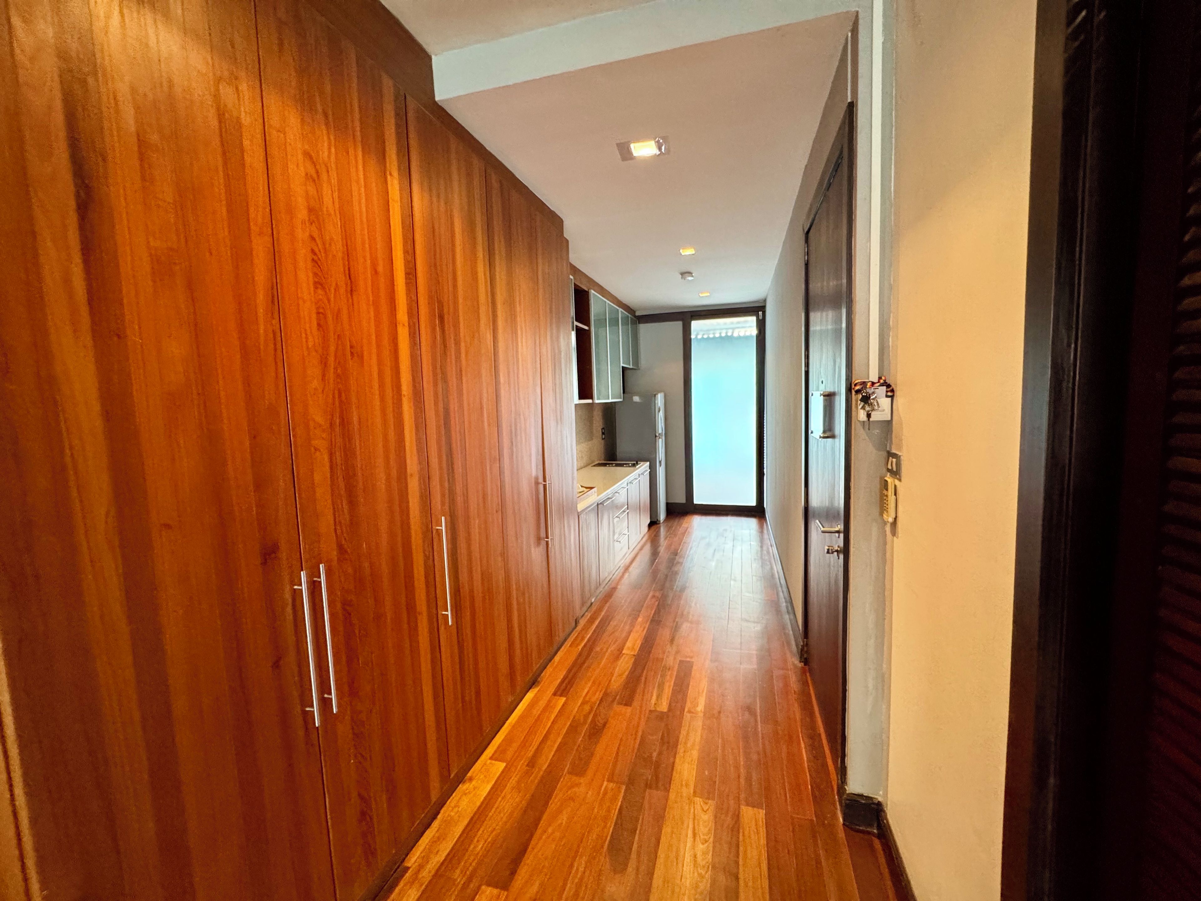 A hallway with wooden flooring and cabinets.