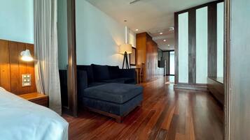 A hotel room with a wooden floor, a sofa, a lamp, and a bed.