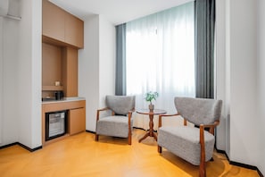 A modern hotel room with a kitchenette, two armchairs, a small round table, and a large window with curtains. - 16KM HOTEL (Dongmakkhai)