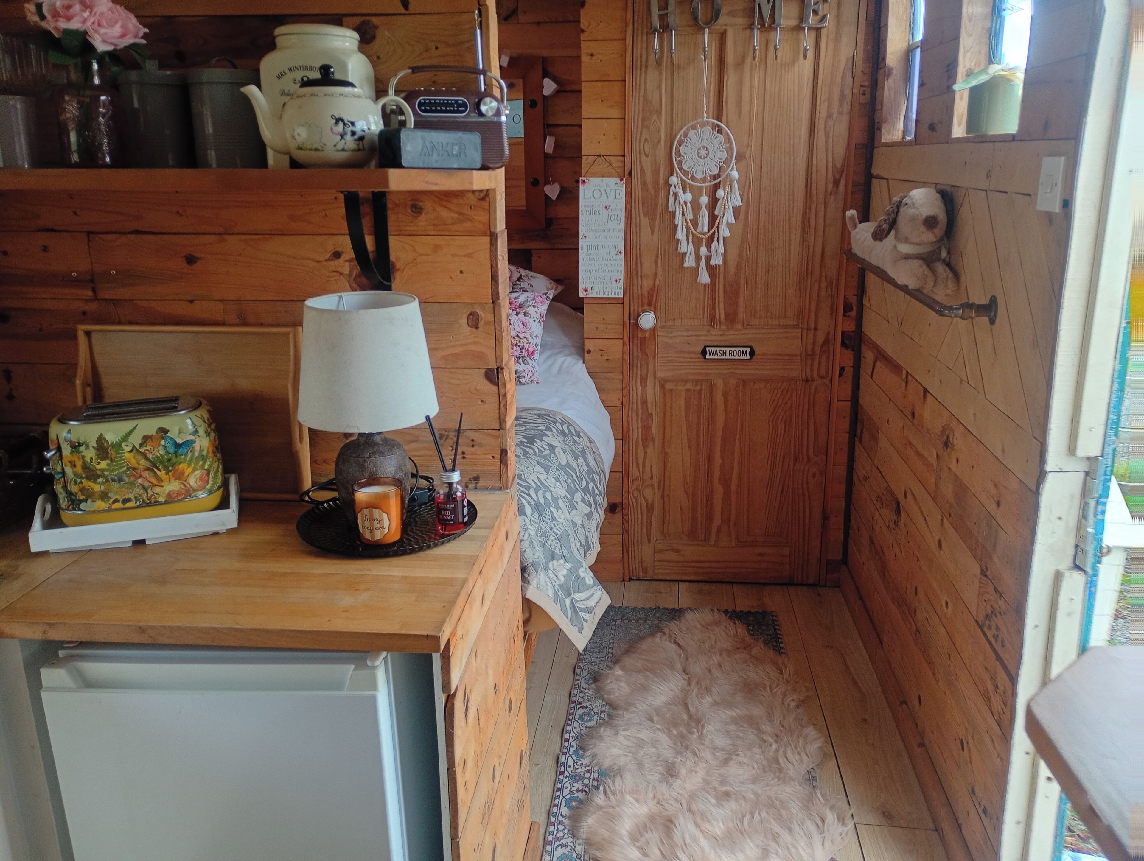 Ein gemütlicher, holzgetäfelter Raum im Blockhausstil mit einem Bett, einem kleinen Tisch mit Lampe, einem Toaster und einem Kühlschrank.