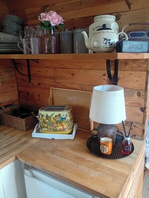 Una estantería de madera con utensilios de cocina, un tostador, una lámpara y una vela.