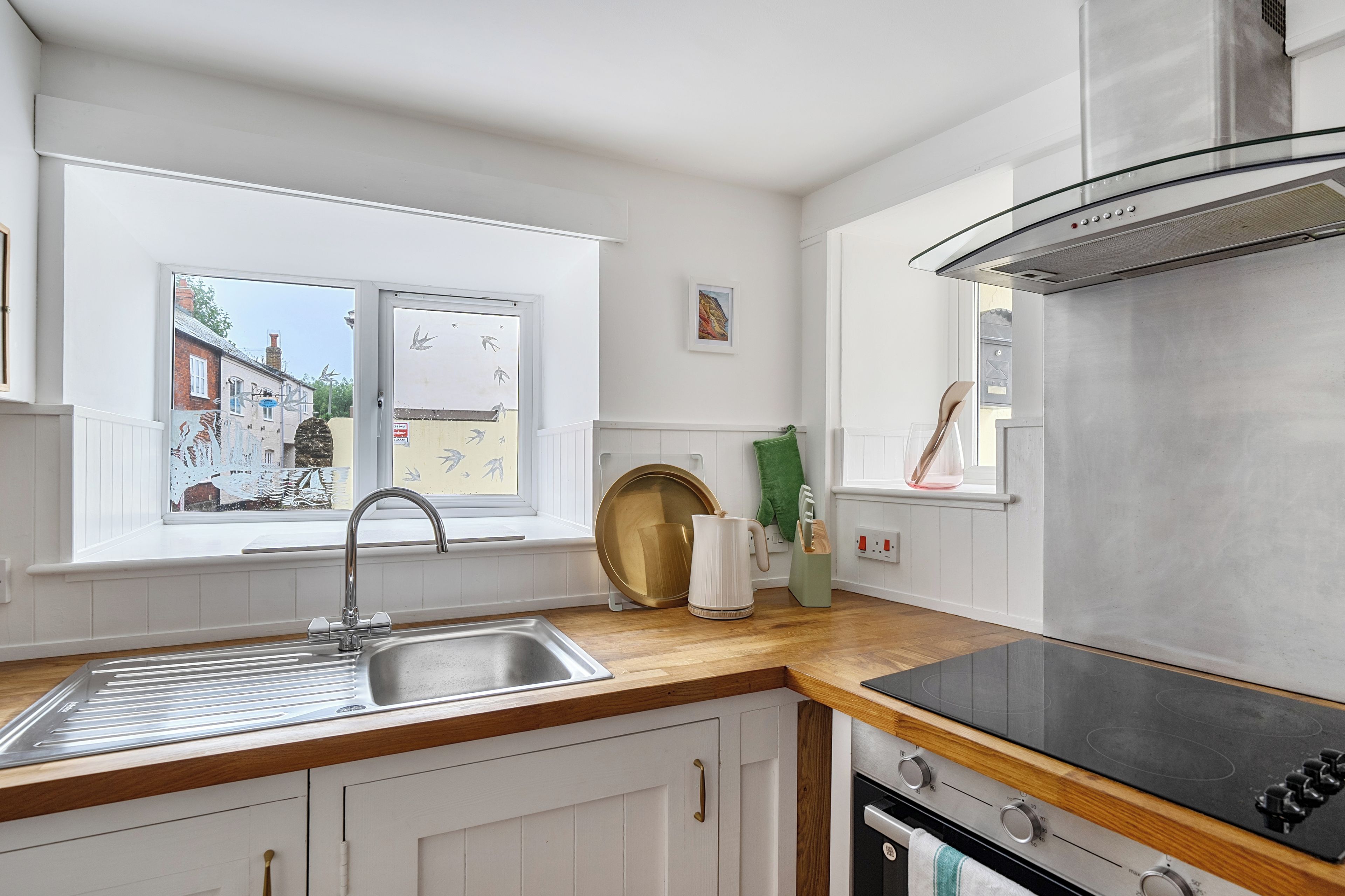 Une cuisine moderne avec un évier en acier inoxydable, une cuisinière noire et une fenêtre donnant sur un immeuble.