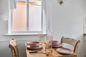 A dining table with pink plates, a glass, and a spoon set. There is a window with white curtains and a view of a building outside.