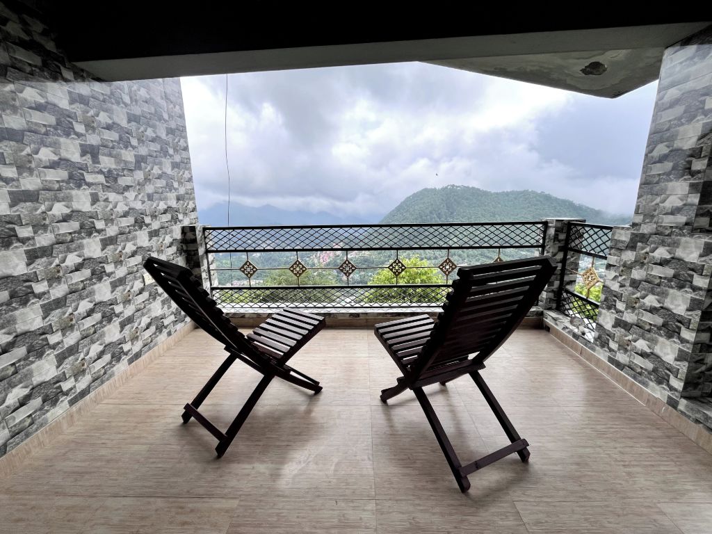 A balcony with two wooden chairs, stone walls, and a view of a mountain.