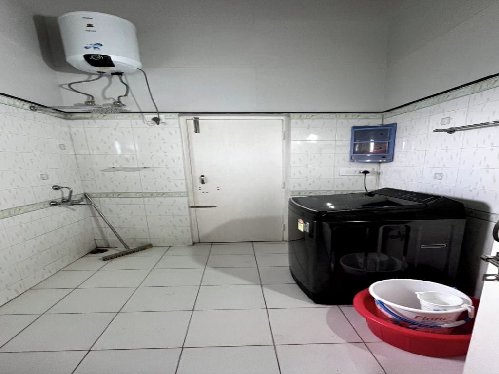 Une petite salle de bain carrelée, avec des toilettes blanches, un lave-linge noir, un lavabo rouge et un radiateur fixé au mur.
