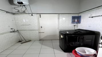 Une petite salle de bain carrelée, avec des toilettes blanches, un lave-linge noir, un lavabo rouge et un radiateur fixé au mur.
