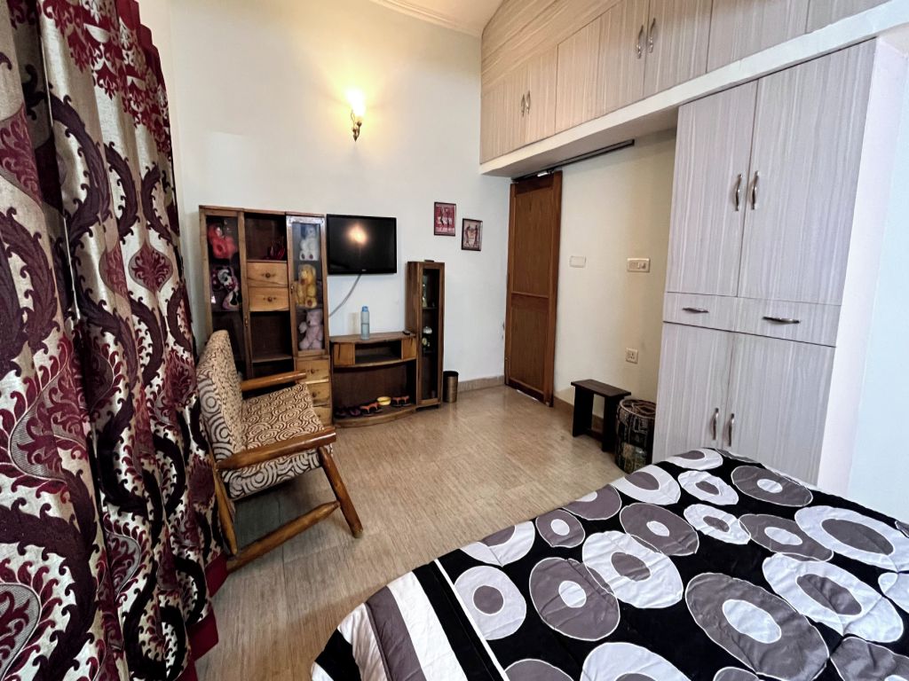 A bedroom with a bed, a wardrobe, a television, and a chair.