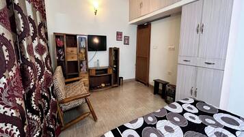 A bedroom with a bed, a wardrobe, a television, and a chair.