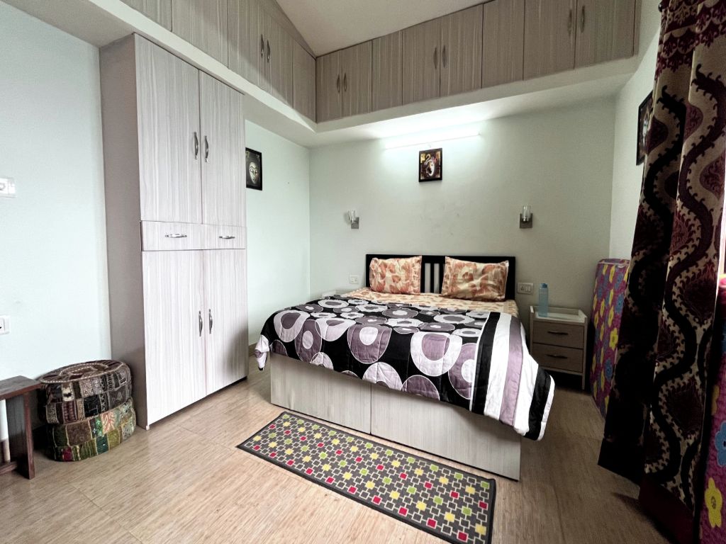 Un dormitorio con cama, armario, mesita de noche y alfombra estampada.