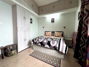 A bedroom with a bed, wardrobe, bedside table, and a patterned rug.